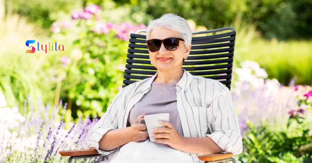 an old age woman wearing goggles having tea in a garden by sitting on a chair