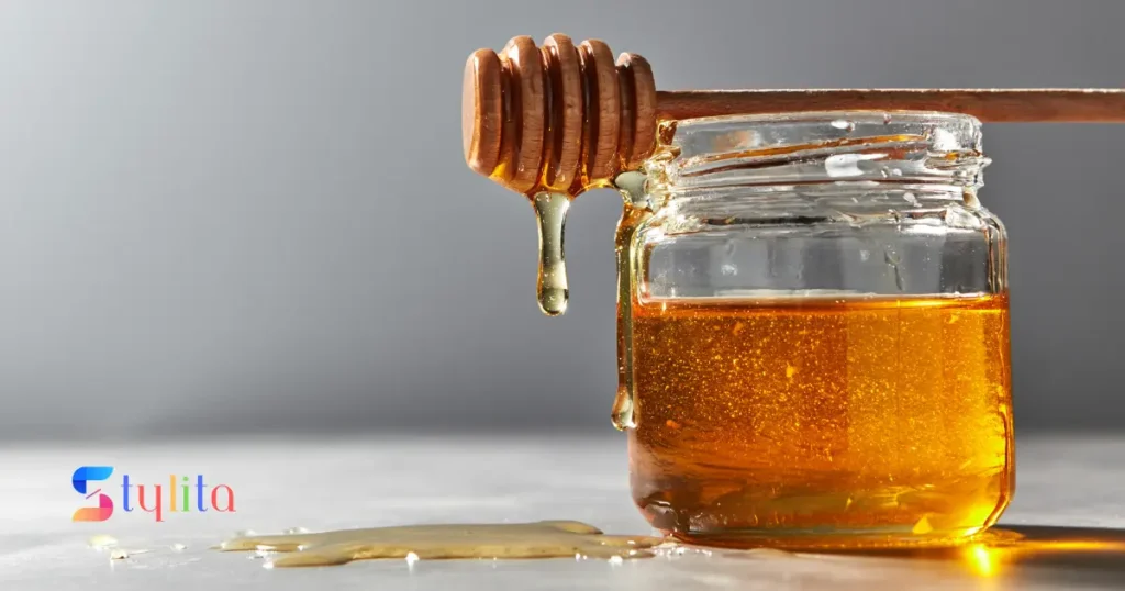 a bottle half filled with honey and honey dripping down by a stick filled with honey