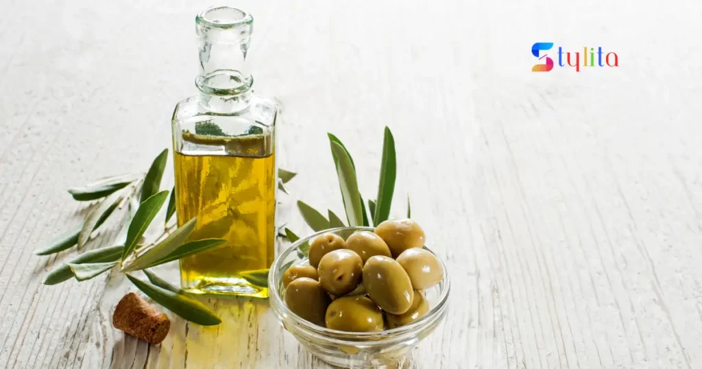 a glass bottle filled with olive oil and a glass bowl placed by side contains olives in it