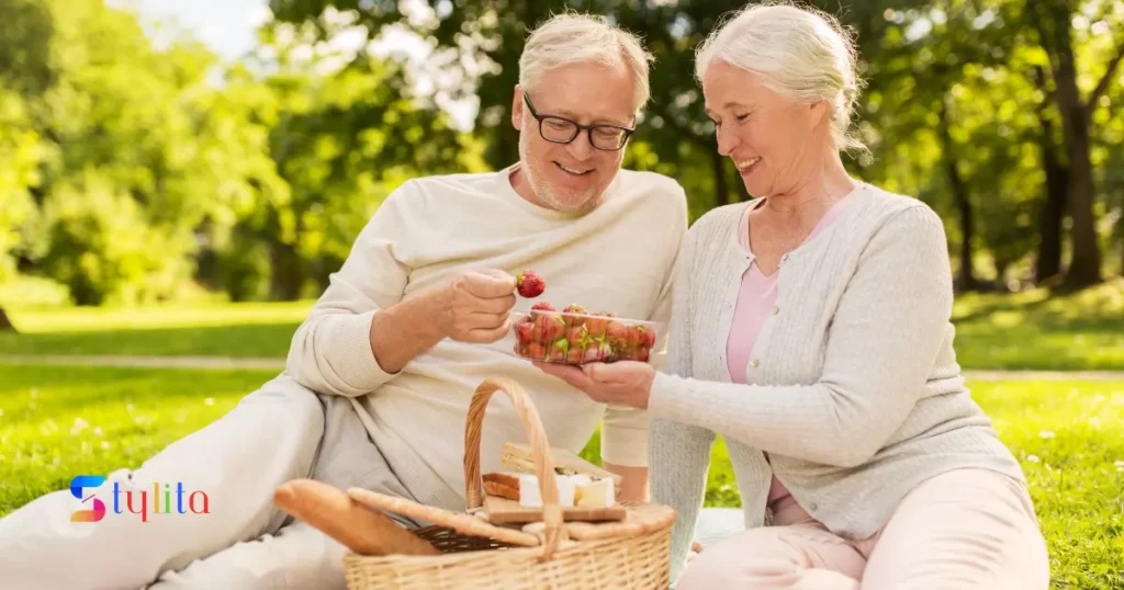 an old couple enjoying picnic in a garden and eating strawberries in a happy mood