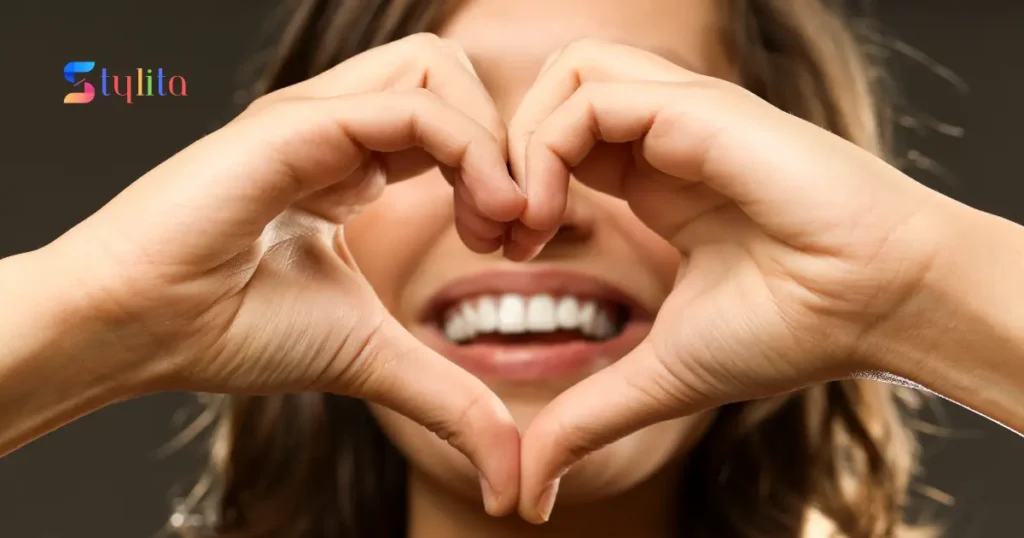 a girl making heart with her hands and her white teeth are shown in between